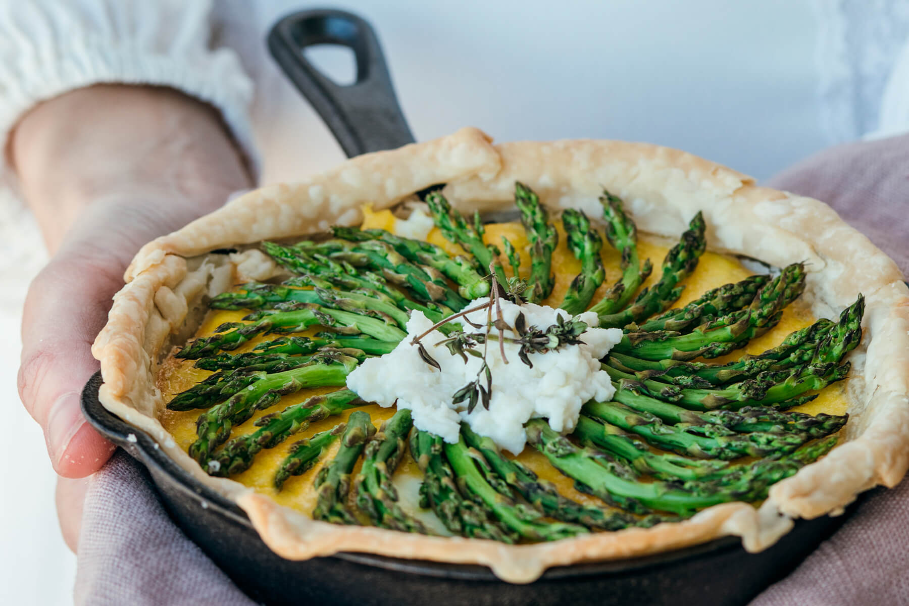 Herzhafte Spargel-Tarte mit rustikalem Mürbeteigrand in einer gusseisernen Pfanne, in Händen gehalten