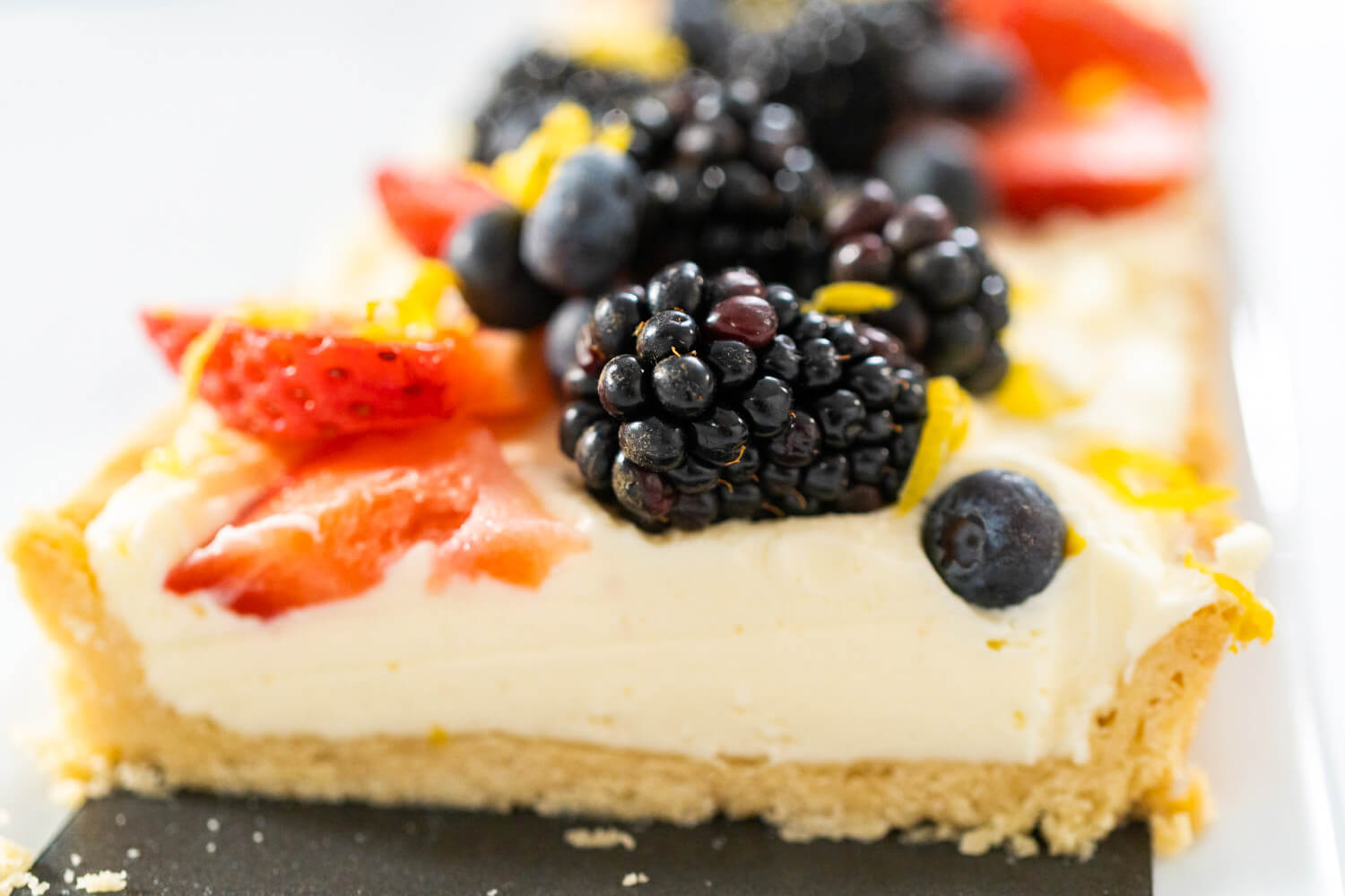 Angeschnittenes Stück süße Tarte mit knusprigem Mürbeteigboden, weißer Mascarponecreme und frischen Beeren