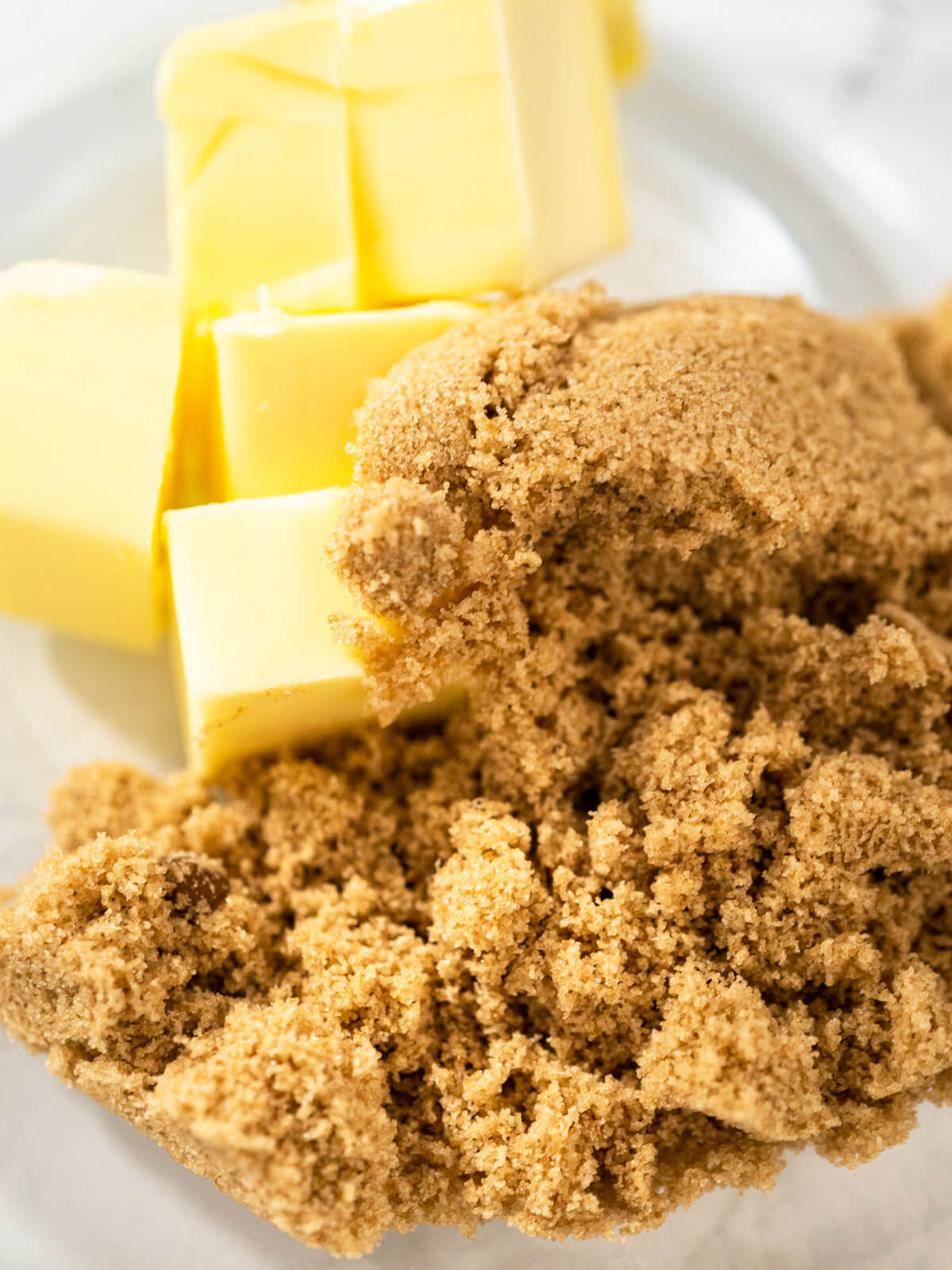 Weiche Butter in Stücken neben einem Häufchen braunem Zucker, bereit zum cremigen Aufschlagen