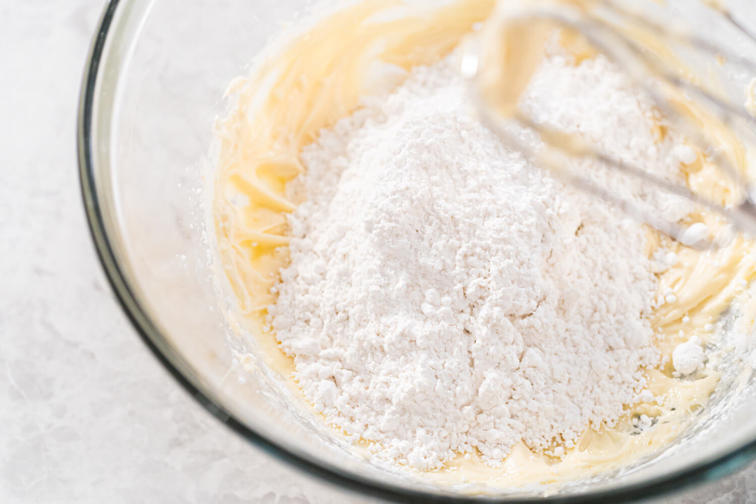 Mehl wird auf die hell aufgeschlagene Butter-Zucker-Ei-Masse in einer Glasschüssel gegeben