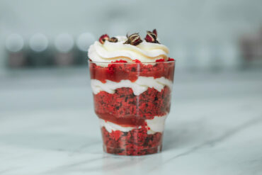 Schichtdessert im Glas von der Seite mit Kuchenkrümeln, weißer Creme und Fruchtpüree