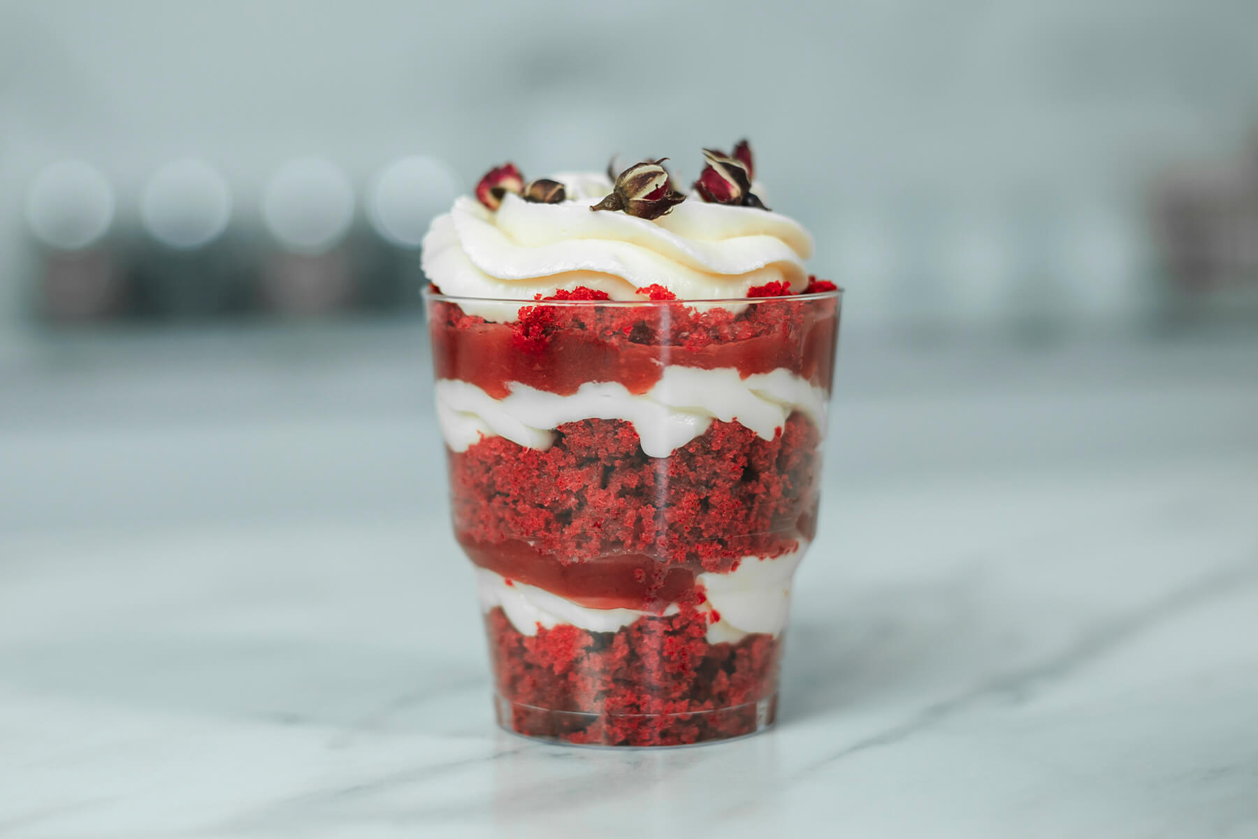 Schichtdessert im Glas von der Seite mit Kuchenkrümeln, weißer Creme und Fruchtpüree