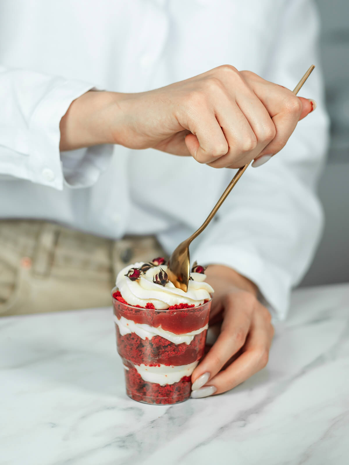 Ein Löffel taucht in die Cremekrone eines Schichtdesserts im Glas