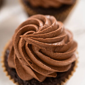 Schokoladen-Cupcake im braunen Papierförmchen mit dichter Rosette aus hellbrauner Schoko-Buttercreme, Nahaufnahme von oben