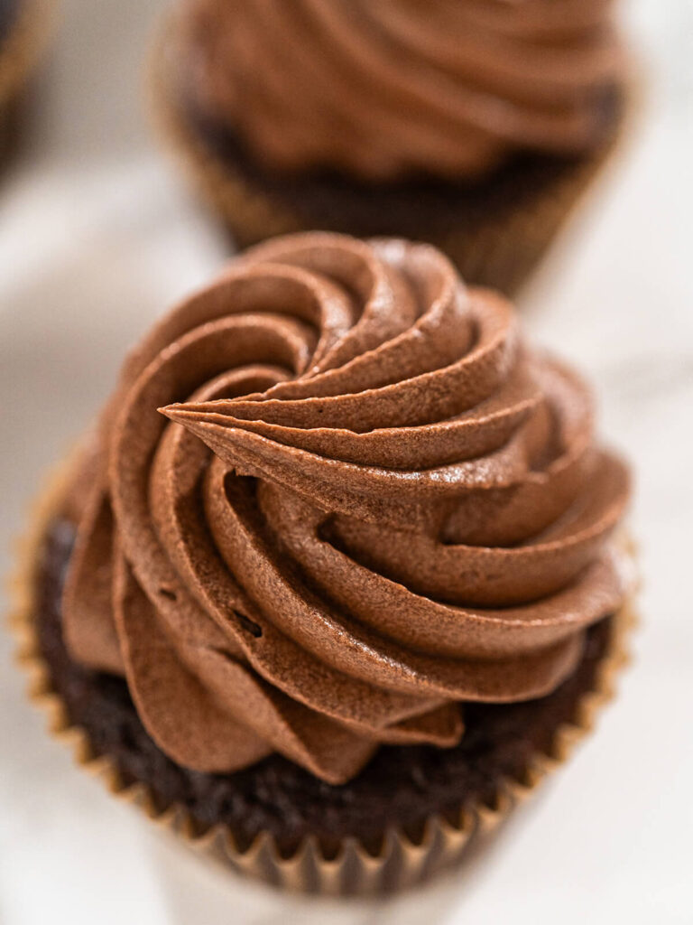 Schokoladen-Cupcake im braunen Papierförmchen mit dichter Rosette aus hellbrauner Schoko-Buttercreme, Nahaufnahme von oben