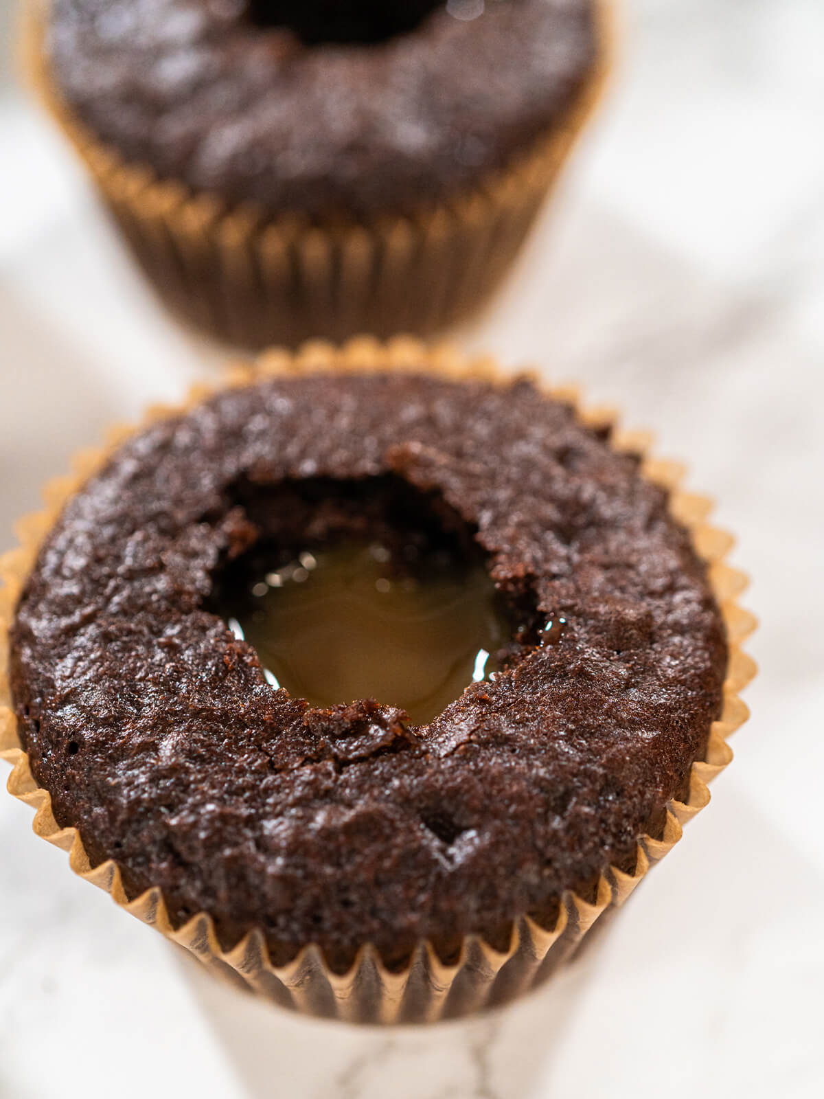 Nahaufnahme eines Schokoladen-Cupcakes mit ausgestochener Mulde, in der hell goldenes Karamell glänzend steht