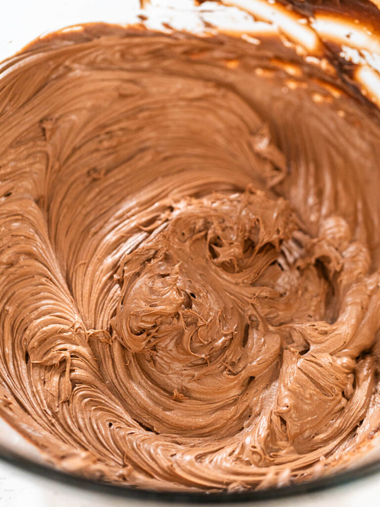 Fertig aufgeschlagene Schoko-Buttercreme in hellem Milchschokoladenbraun mit seidigen Wellen in einer Rührschüssel