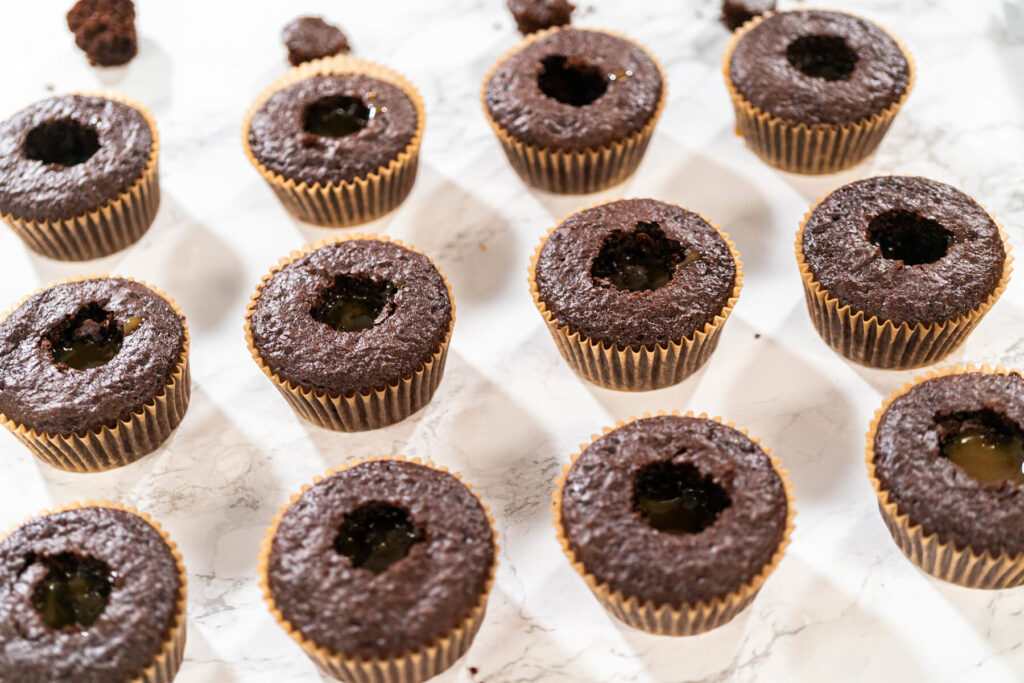 Zwölf Schokoladen-Cupcakes, deren Mulden mit hell goldenem, glänzendem Karamell gefüllt sind
