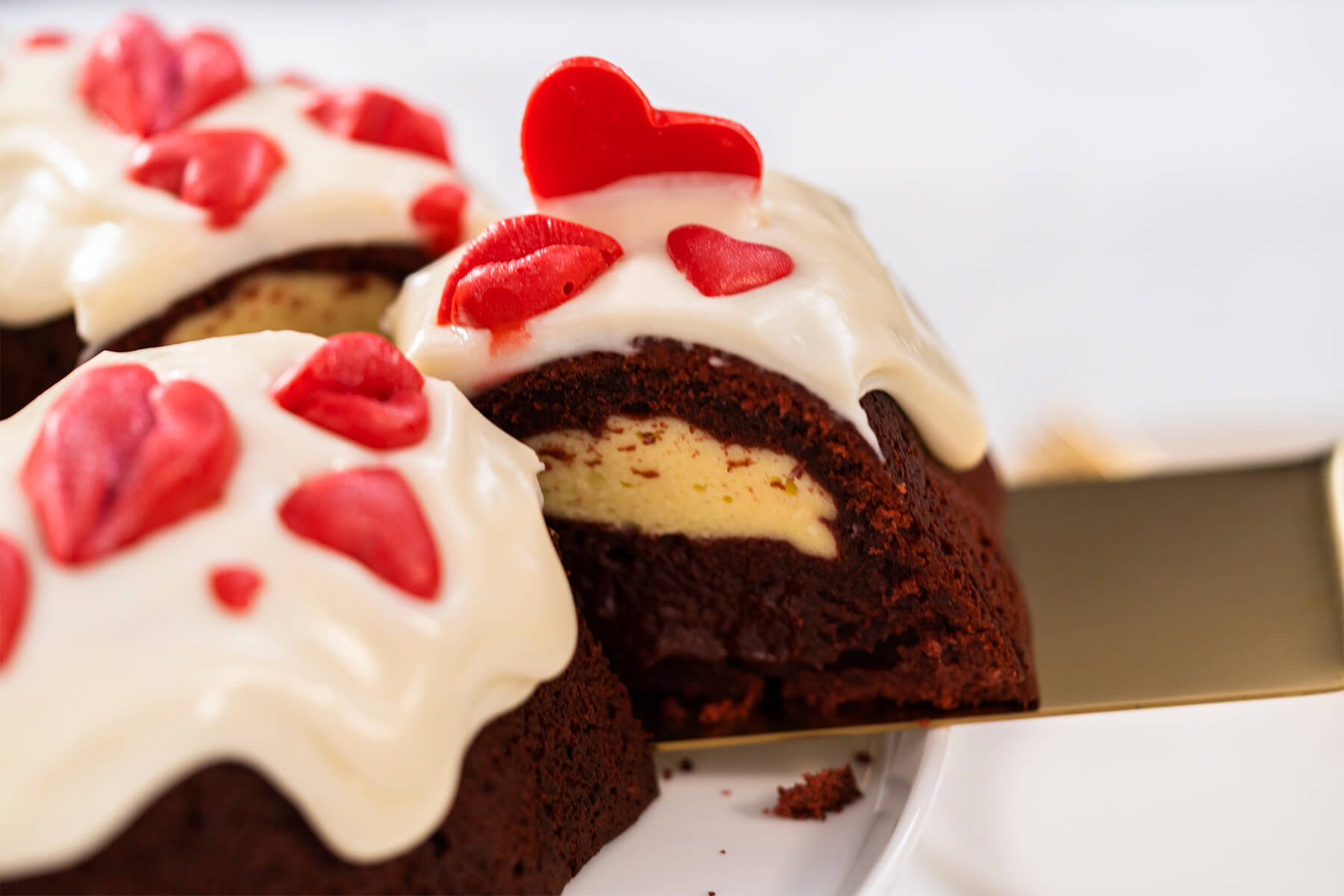 Kuchenstück mit großem roten Schoko-Herz wird von einem glasierten Gugelhupf gehoben