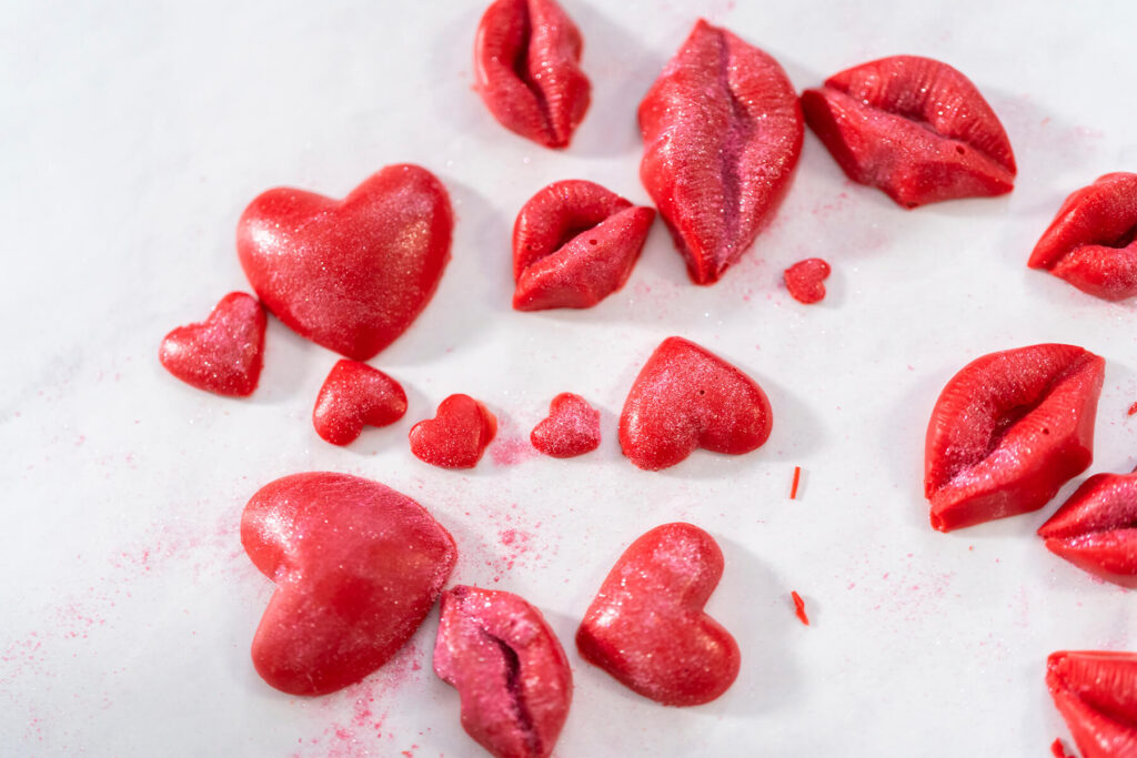 Fertige rote Schoko-Herzen und Schoko-Lippen mit Perlmuttschimmer auf weißem Backpapier
