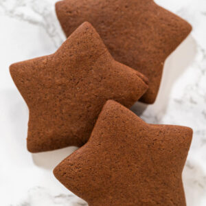 Drei gebackene Schoko-Lebkuchen-Sterne mit sauberen Kanten auf einer weißen Marmorfläche