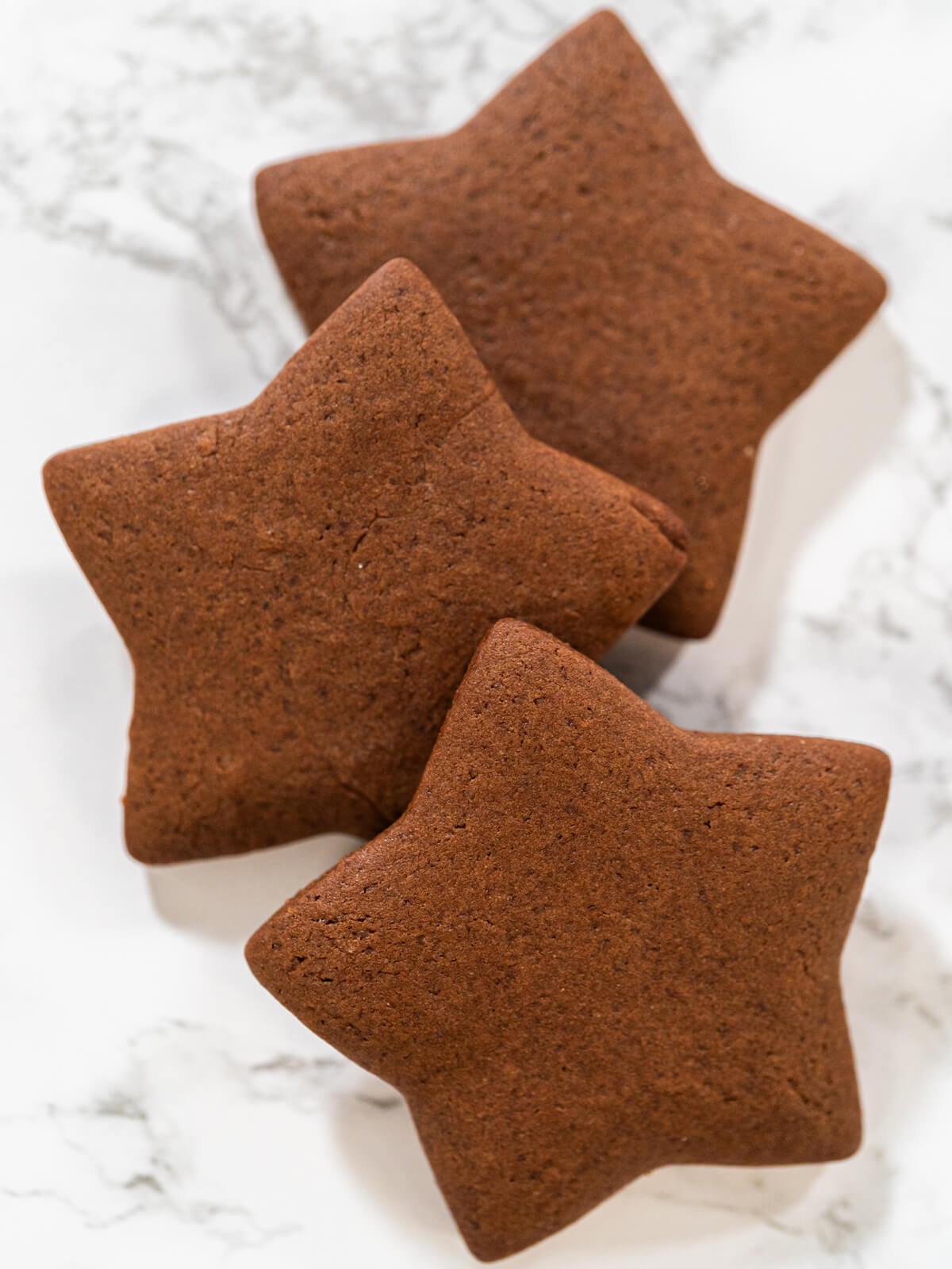 Drei gebackene Schoko-Lebkuchen-Sterne mit sauberen Kanten auf einer weißen Marmorfläche
