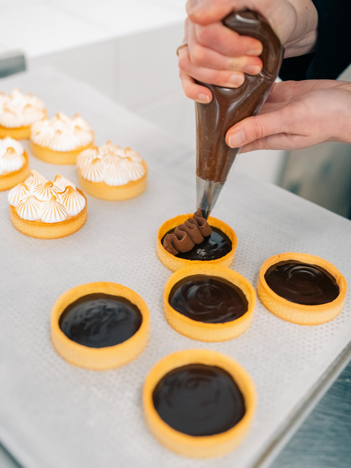 Aus einem Spritzbeutel wird Schokoladencreme in Schlangenlinien auf ein mit fester Ganache gefülltes Tartelette gesetzt
