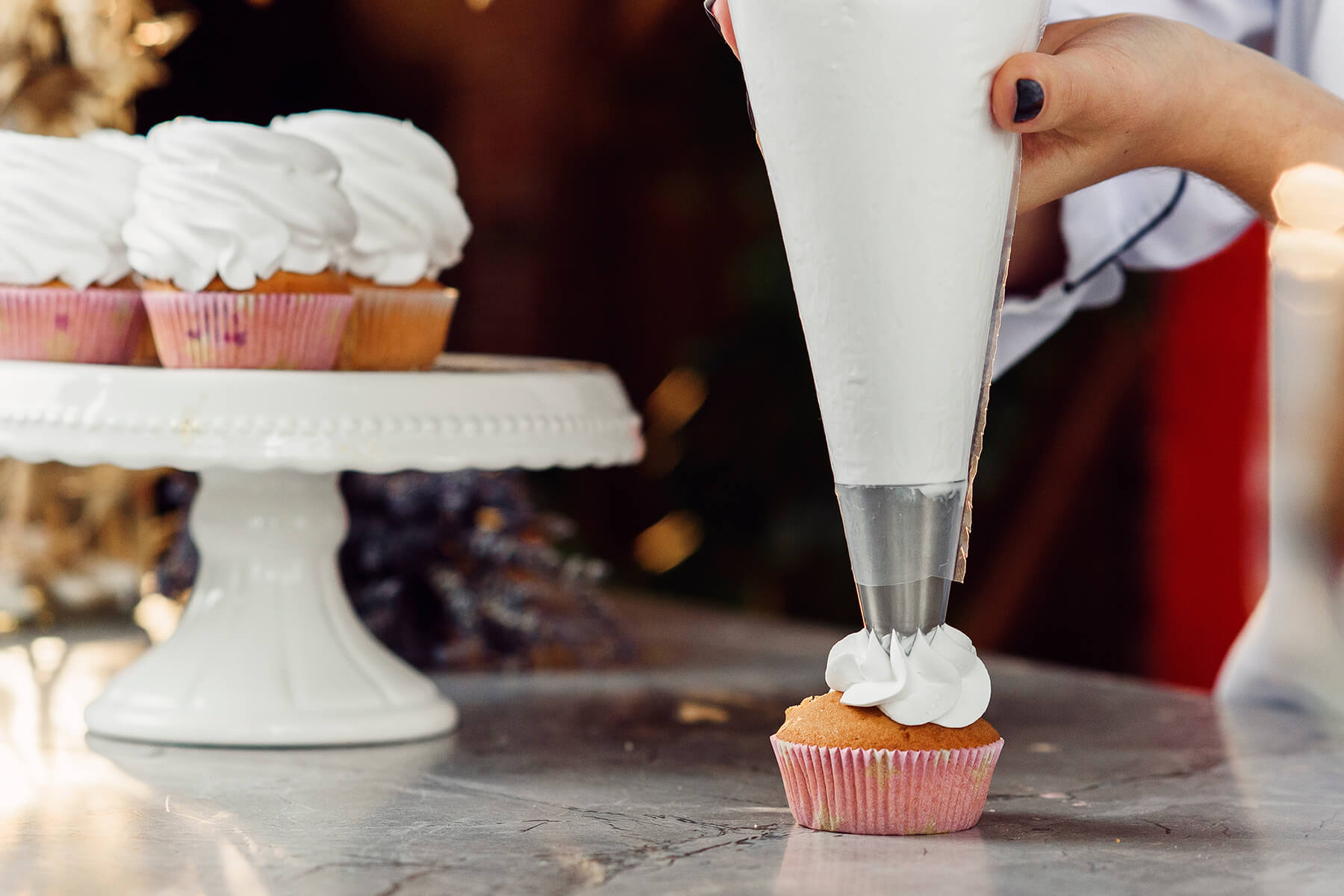 Ein senkrecht gehaltener Spritzbeutel setzt die erste Portion weißer Creme mittig auf ein Gebäckstück
