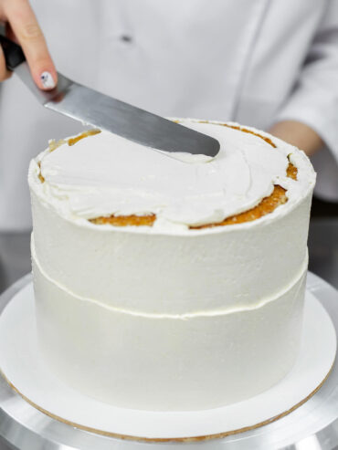 Lange gerade Streichpalette liegt flach auf der Creme einer weiß eingestrichenen Torte und verteilt sie zur Mitte