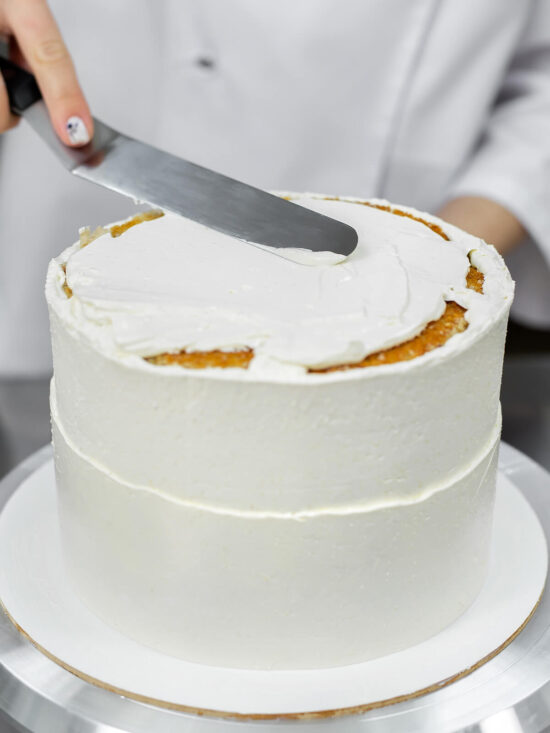 Lange gerade Streichpalette liegt flach auf der Creme einer weiß eingestrichenen Torte und verteilt sie zur Mitte