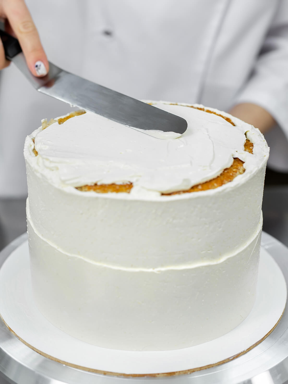 Lange gerade Streichpalette liegt flach auf der Creme einer weiß eingestrichenen Torte und verteilt sie zur Mitte