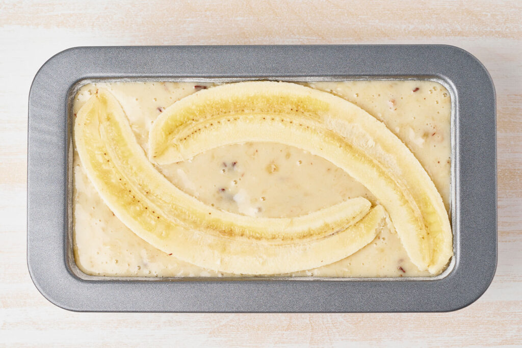 Weicher Walnussteig in der Kastenform, belegt mit drei längs halbierten Bananen in versetzten Bögen