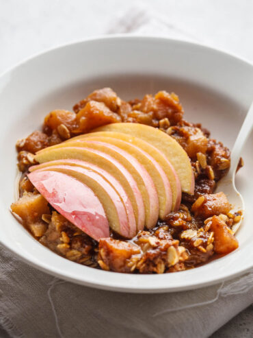 Glutenfreier Apfel-Crisp mit Haferflocken in einer weißen Schale, obenauf ein Fächer aus dünnen Apfelscheiben