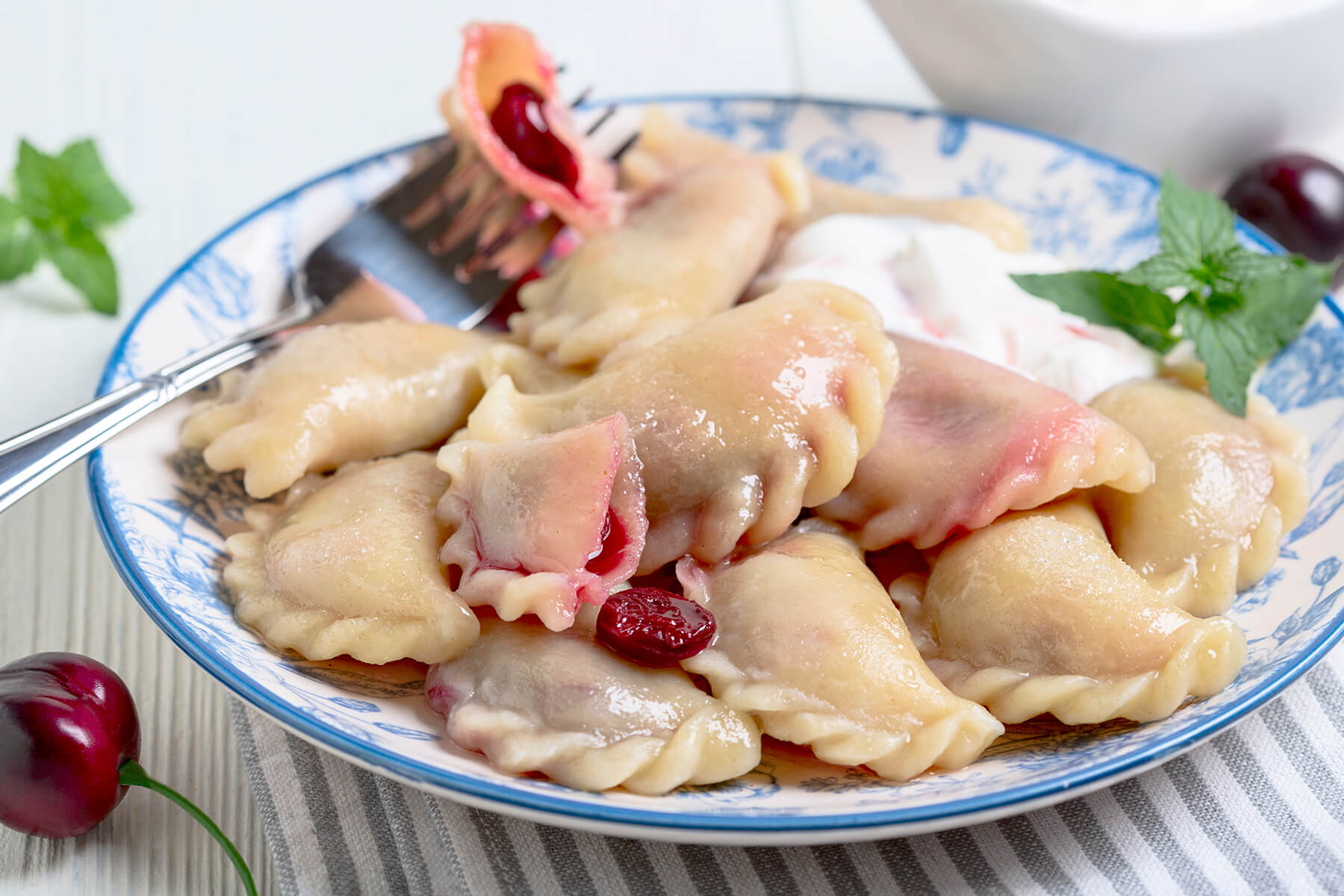 Gekochte Kirsch-Vareniki mit glänzender Zopf-Naht, dazu Sauerrahm und frische Minze