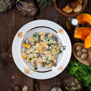 Teller mit orangefarbenen Kürbisgnocchi, Steinpilzscheiben, heller Sauce und Blauschimmelkäse von oben