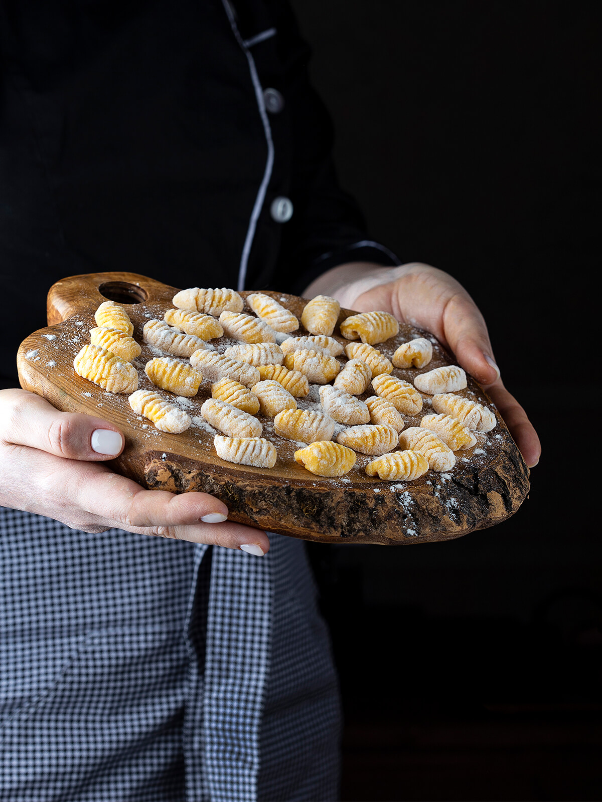 Ein Holzbrett mit rohen Kürbisgnocchi wird in beiden Händen gehalten