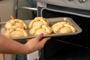 Ein Backblech mit glänzend eingepinselten Pan de Muerto wird in den geöffneten Backofen geschoben