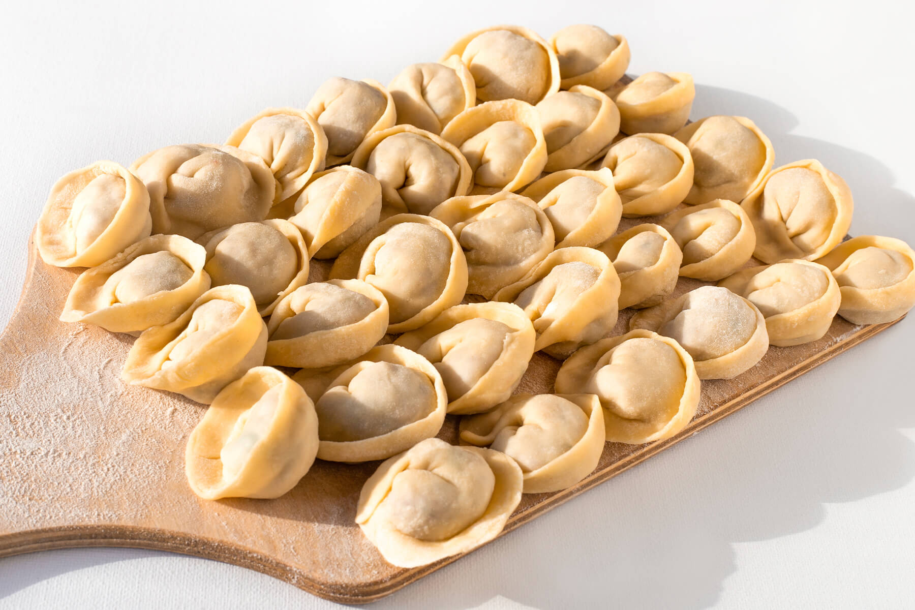 Rohe Pelmeni in Öhrchenform dicht nebeneinander auf einem bemehlten Holzbrett