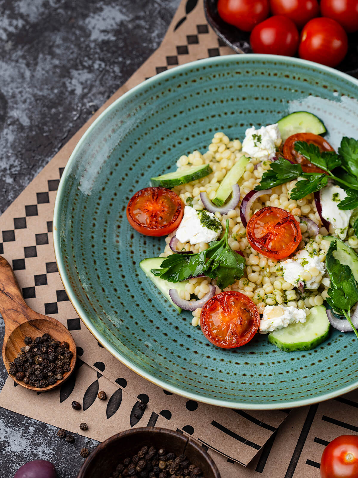 Nahaufnahme des Perlnudel-Salats mit Feta-Stücken, gebratenen Tomaten und grünem Petersilienöl