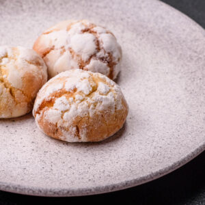 Weiche Amaretti Morbidi mit Puderzucker und gerissener Kruste auf einem hellen Teller