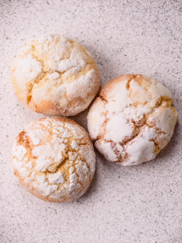Nahaufnahme von drei Amaretti Morbidi mit gerissener Puderzuckerkruste
