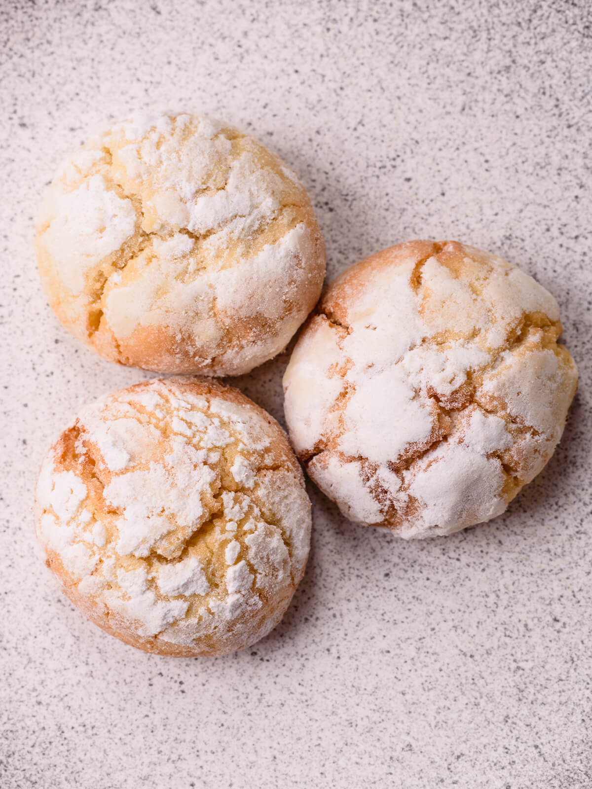 Nahaufnahme von drei Amaretti Morbidi mit gerissener Puderzuckerkruste