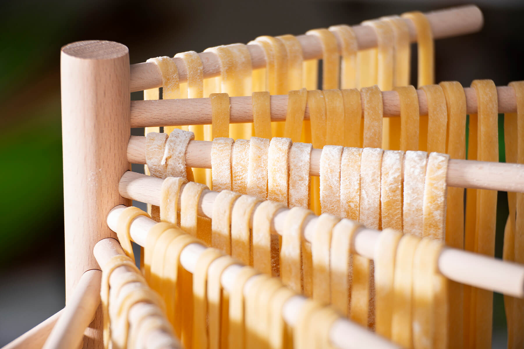 Frische Bandnudeln hängen einzeln nebeneinander über den Holzstäben eines Trockenständers