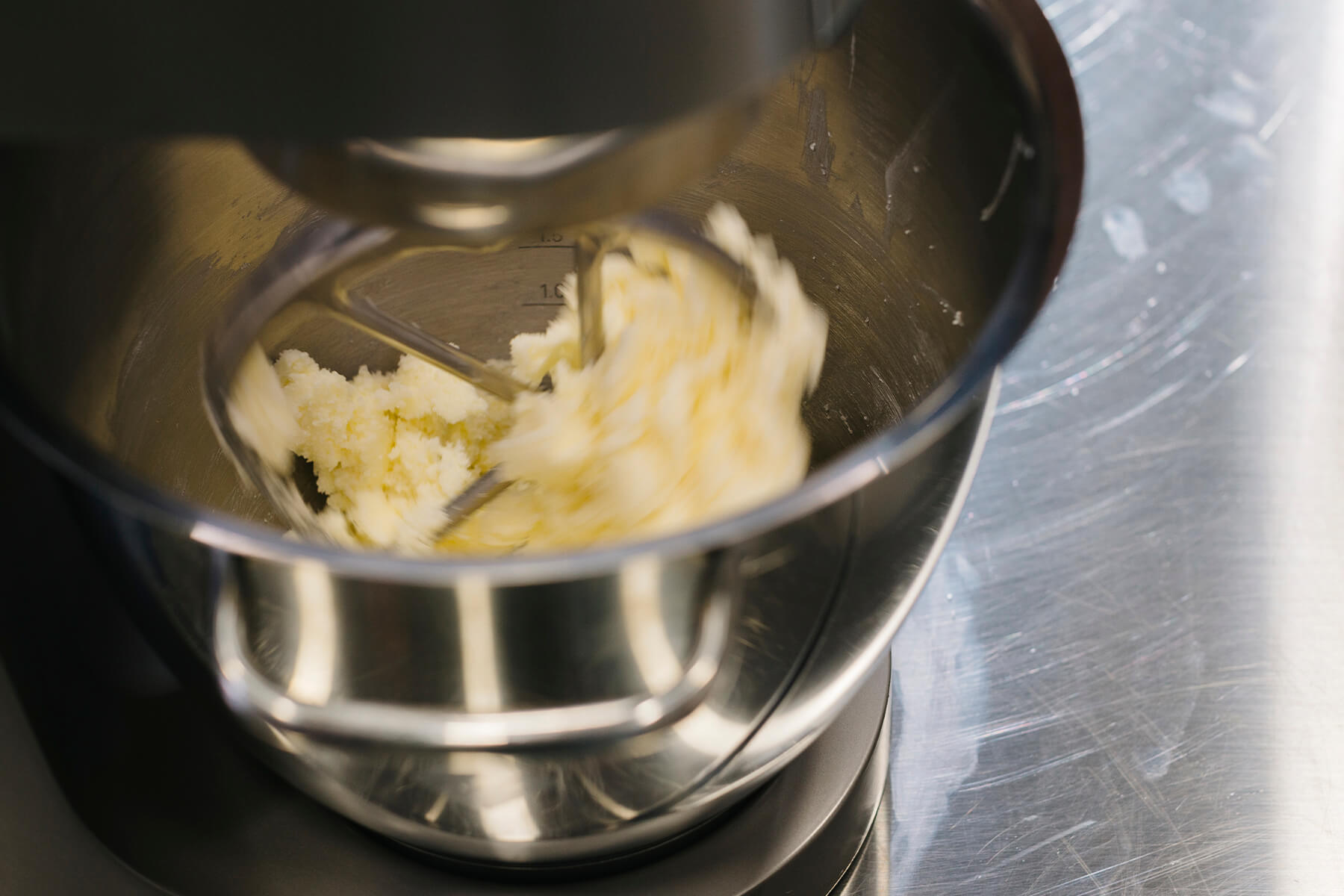 In der Rührschüssel einer Küchenmaschine liegt eine helle Buttermasse, links noch körnig und rechts bereits glatt gestrichen