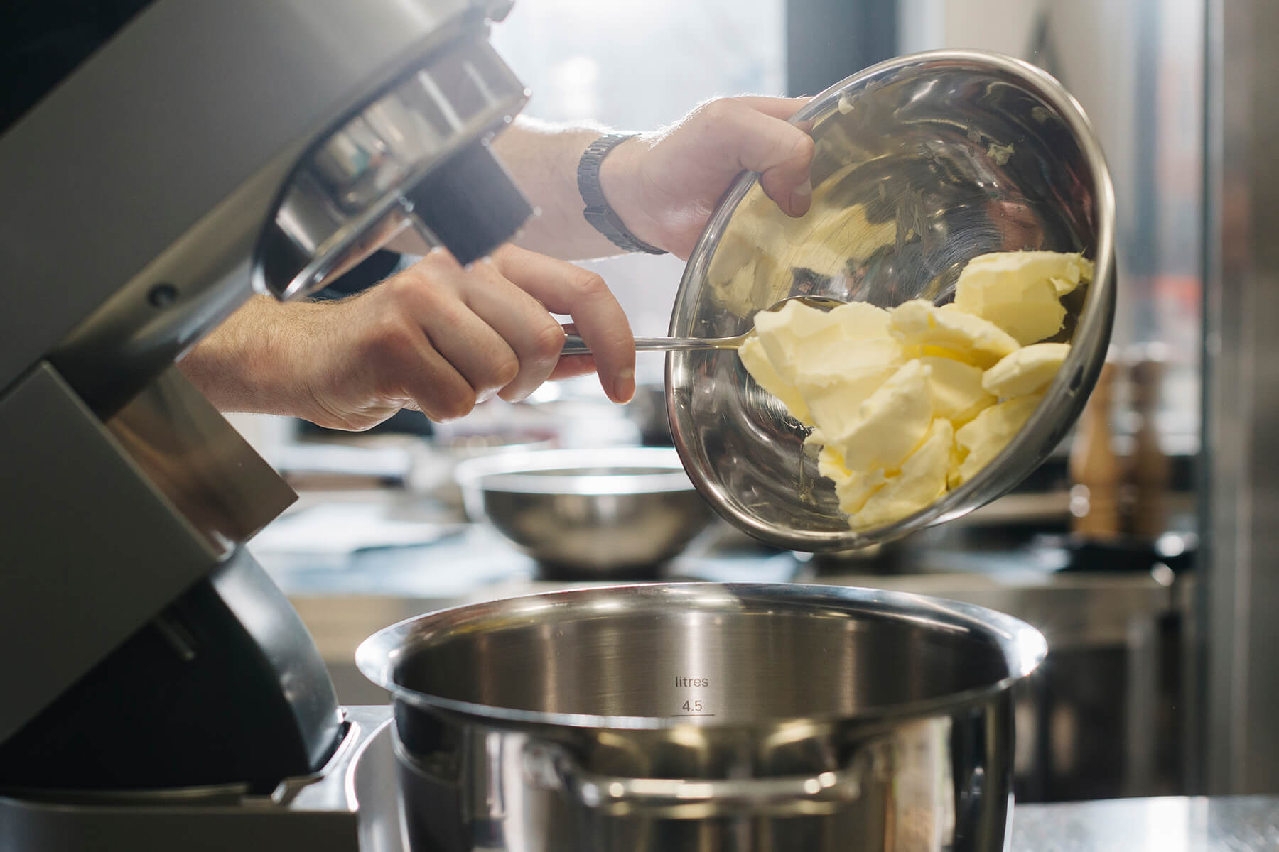 Aus einer Schüssel werden große Stücke weiche Butter in die leere Rührschüssel einer Küchenmaschine gegeben