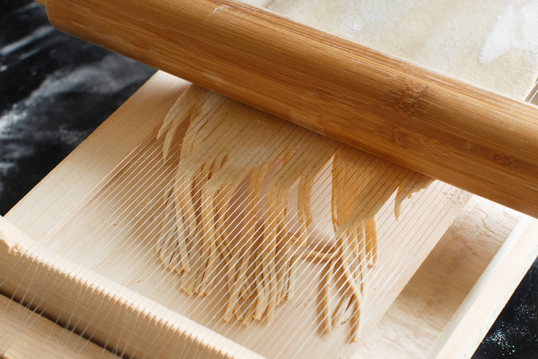 Fertig geschnittene Teigstränge hängen zwischen den Saiten einer Chitarra, ein Teil ist bereits in den Auffangkasten gefallen