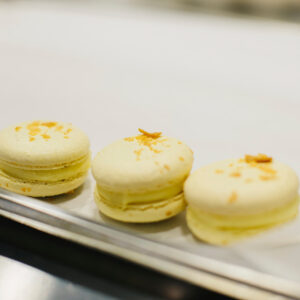 Drei fertige Macarons stehen nebeneinander auf einem Blech, jeder mit glatter Haube, gekräuseltem Fuß und einer sichtbaren Cremeschicht dazwischen
