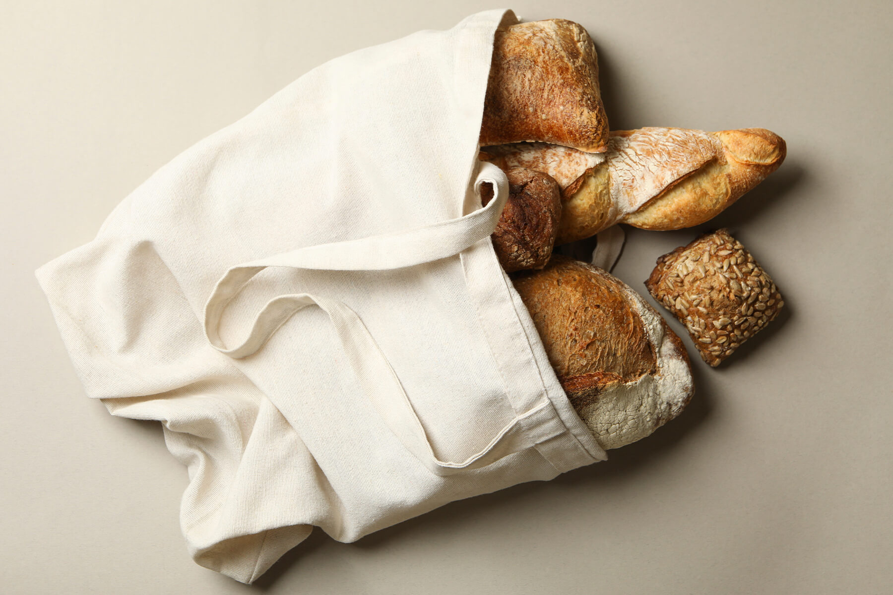 Aufsicht auf einen Baumwollbeutel, aus dem mehrere verschiedene Brote und Brötchen herausschauen