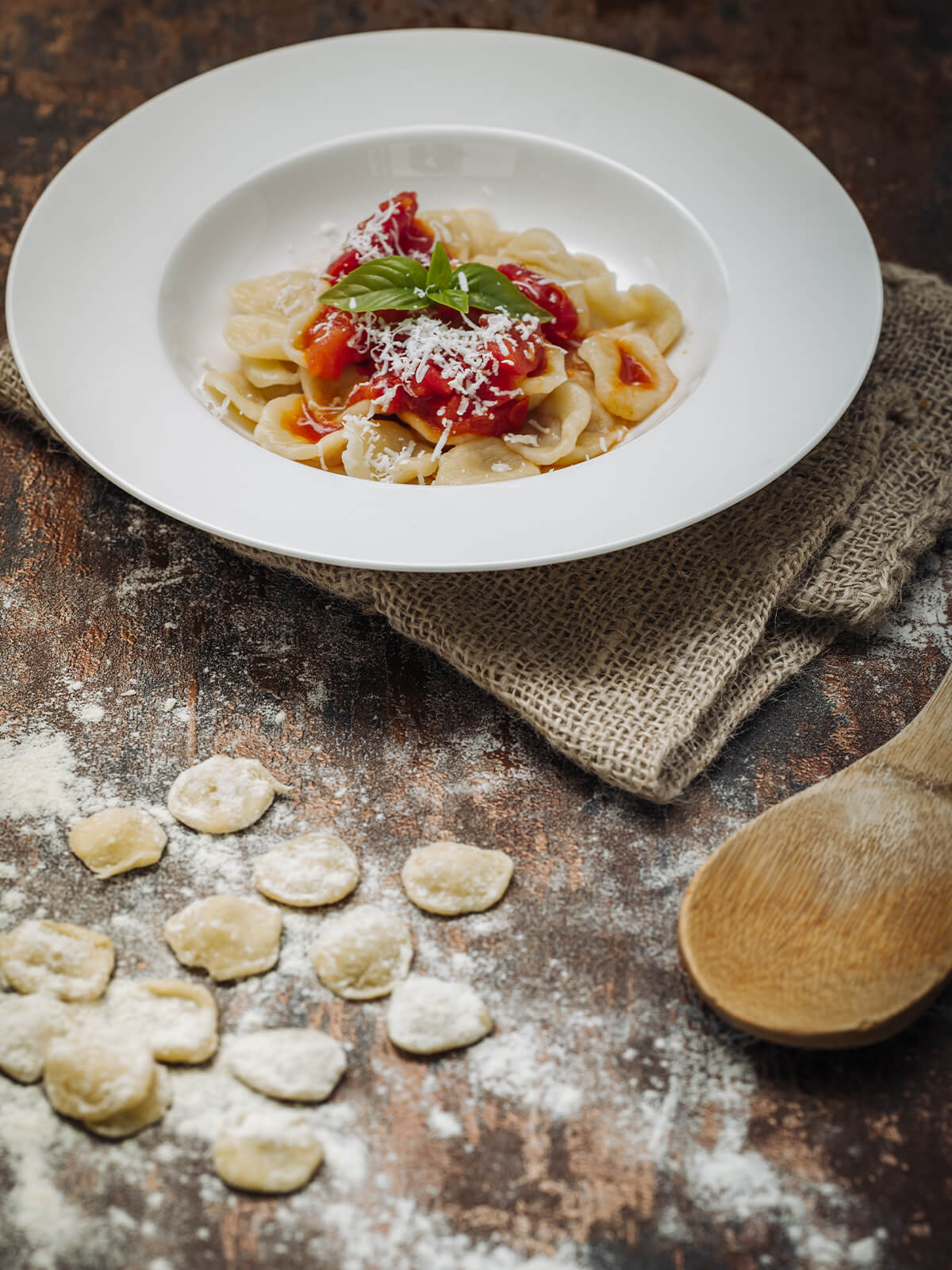 Nahaufnahme frisch geformter Orecchiette mit rauer Innenseite und erhöhtem Rand auf bemehlter dunkler Fläche