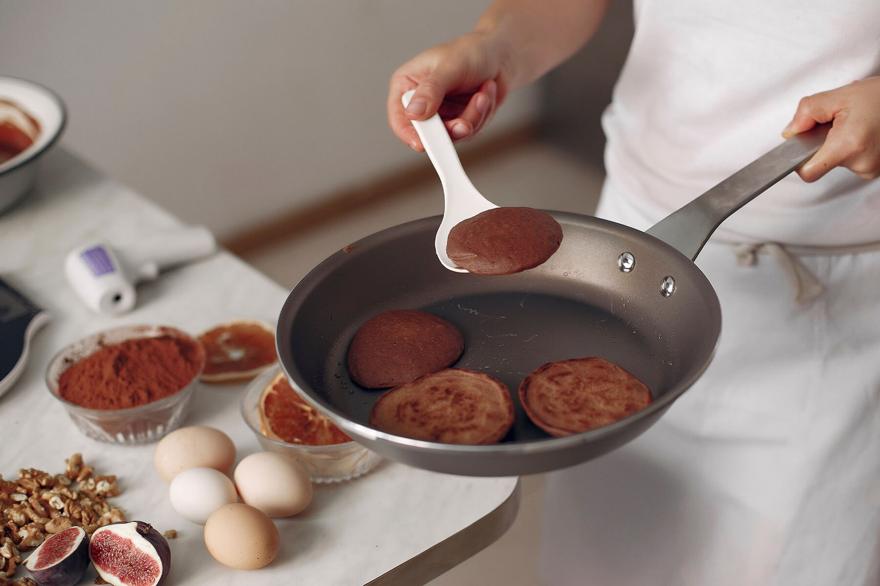 Ein dunkler Pfannkuchen liegt flach auf einem weißen Wender über der Pfanne, seine Oberfläche ist gleichmäßig matt und ohne Bräunungsflecken