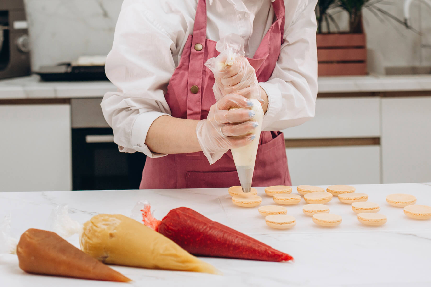 Ein gefüllter Spritzbeutel ist oberhalb der Creme eingedreht und liegt in der Faust, im Vordergrund liegen drei weitere gefüllte Beutel in verschiedenen Farben
