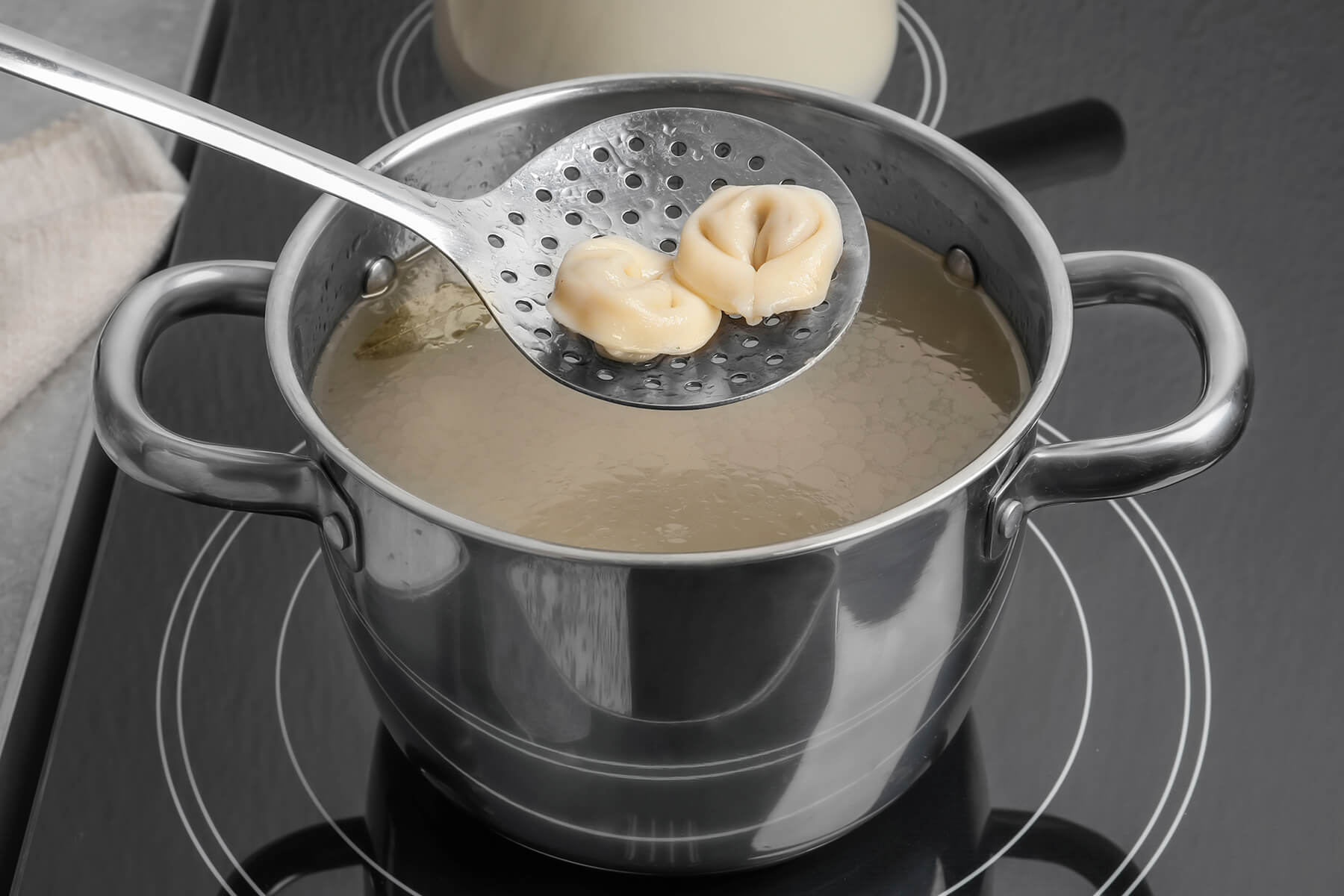 Zwei gegarte Pelmeni auf einer Schaumkelle über einem Topf mit Kochwasser, darin ein Lorbeerblatt