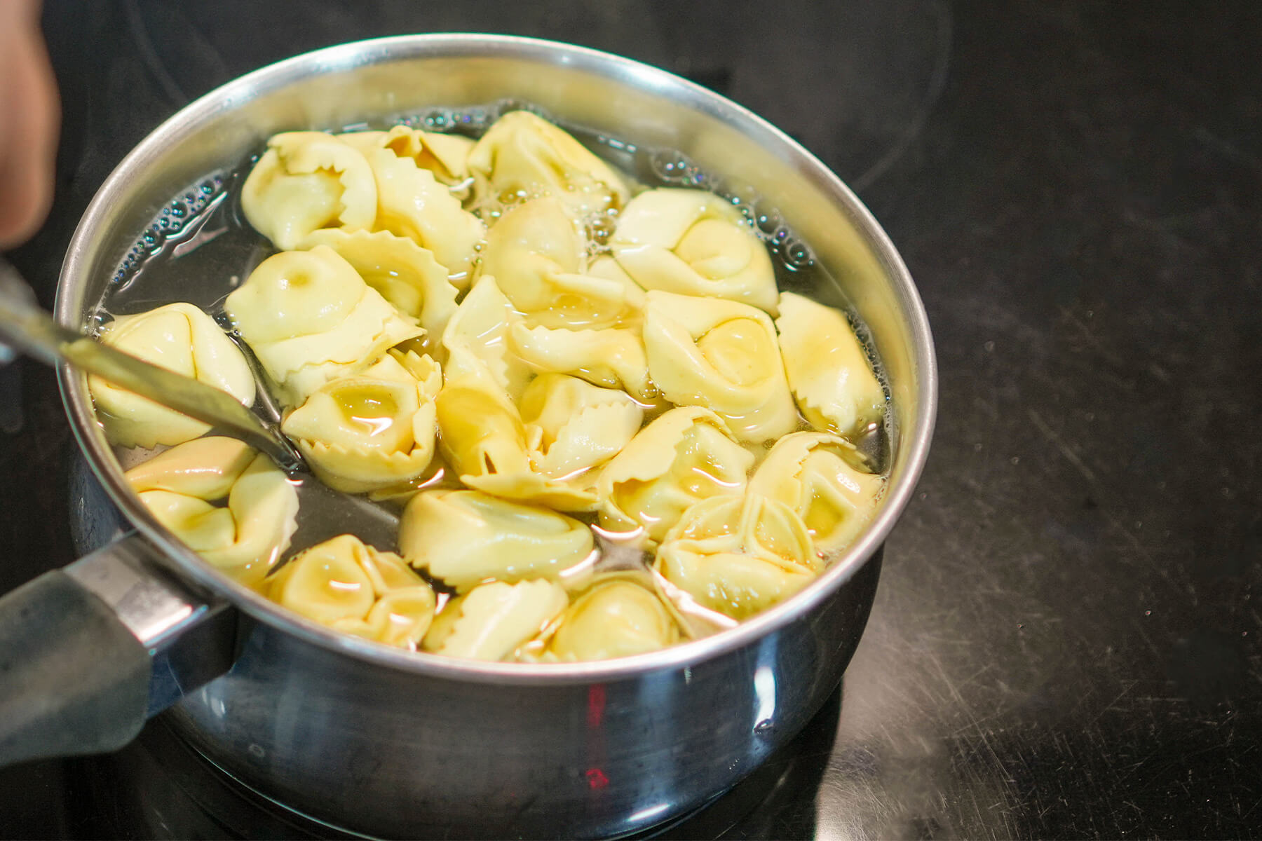 Ein kleiner Stieltopf ist bis an den Rand mit Tortellini gefüllt, die im Wasser dicht aneinanderliegen