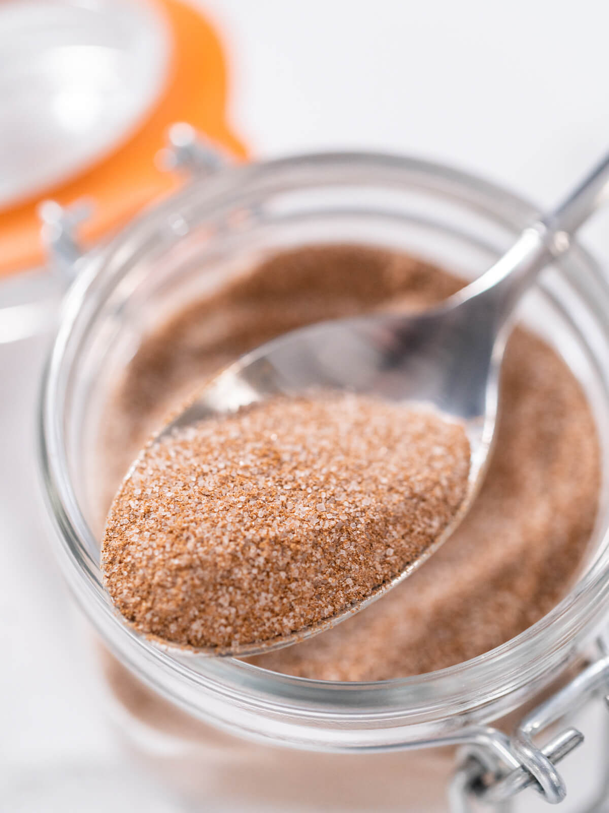 Löffel mit fertigem Zimt-Zucker über einem offenen Bügelglas, die einzelnen Zuckerkristalle sind zwischen dem braunen Zimtpulver deutlich zu erkennen