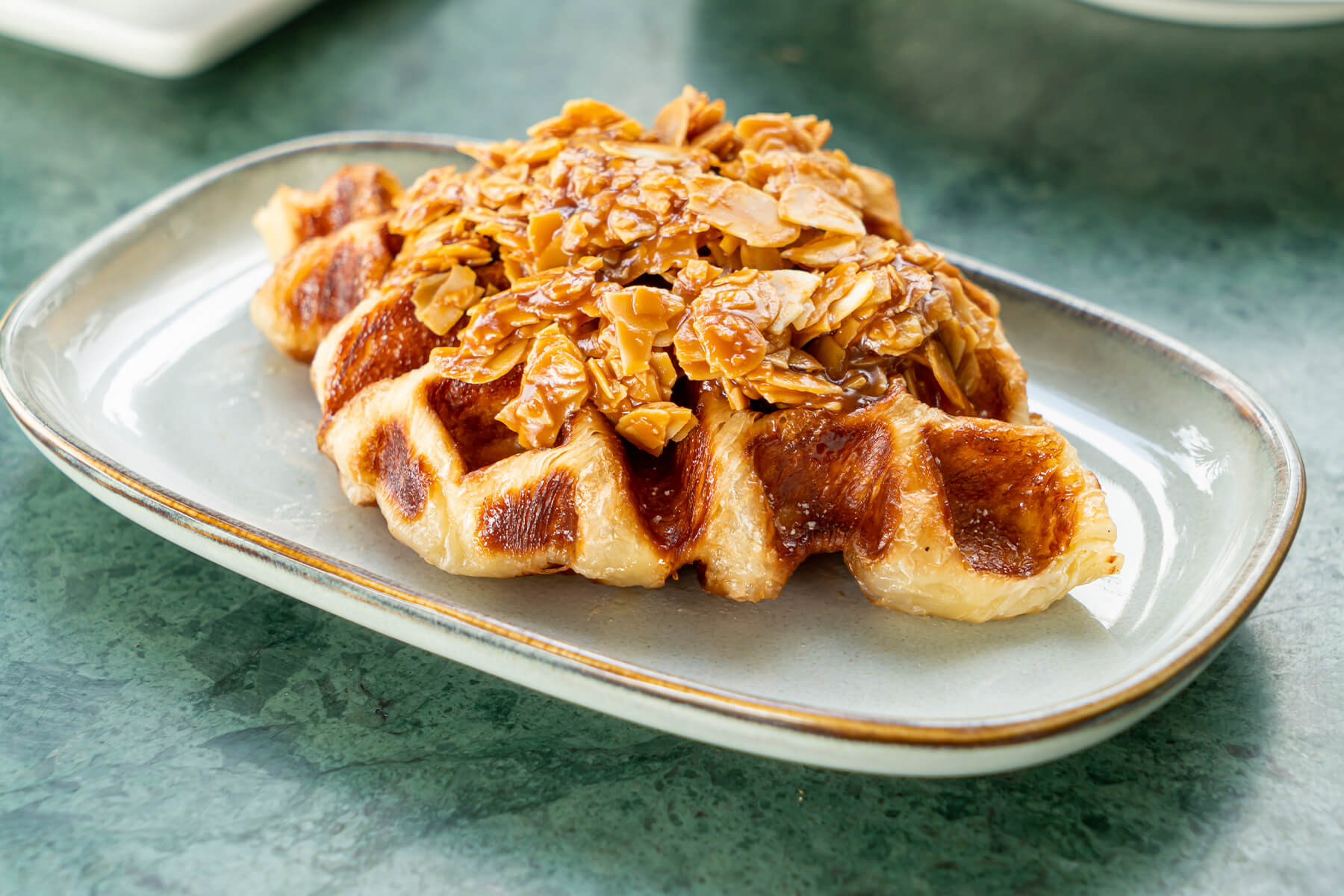 Croissant aus dem Waffeleisen mit karamellisierten Waffelfeldern und hellen, blättrigen Rändern, darauf Mandelblättchen in glänzendem Karamell