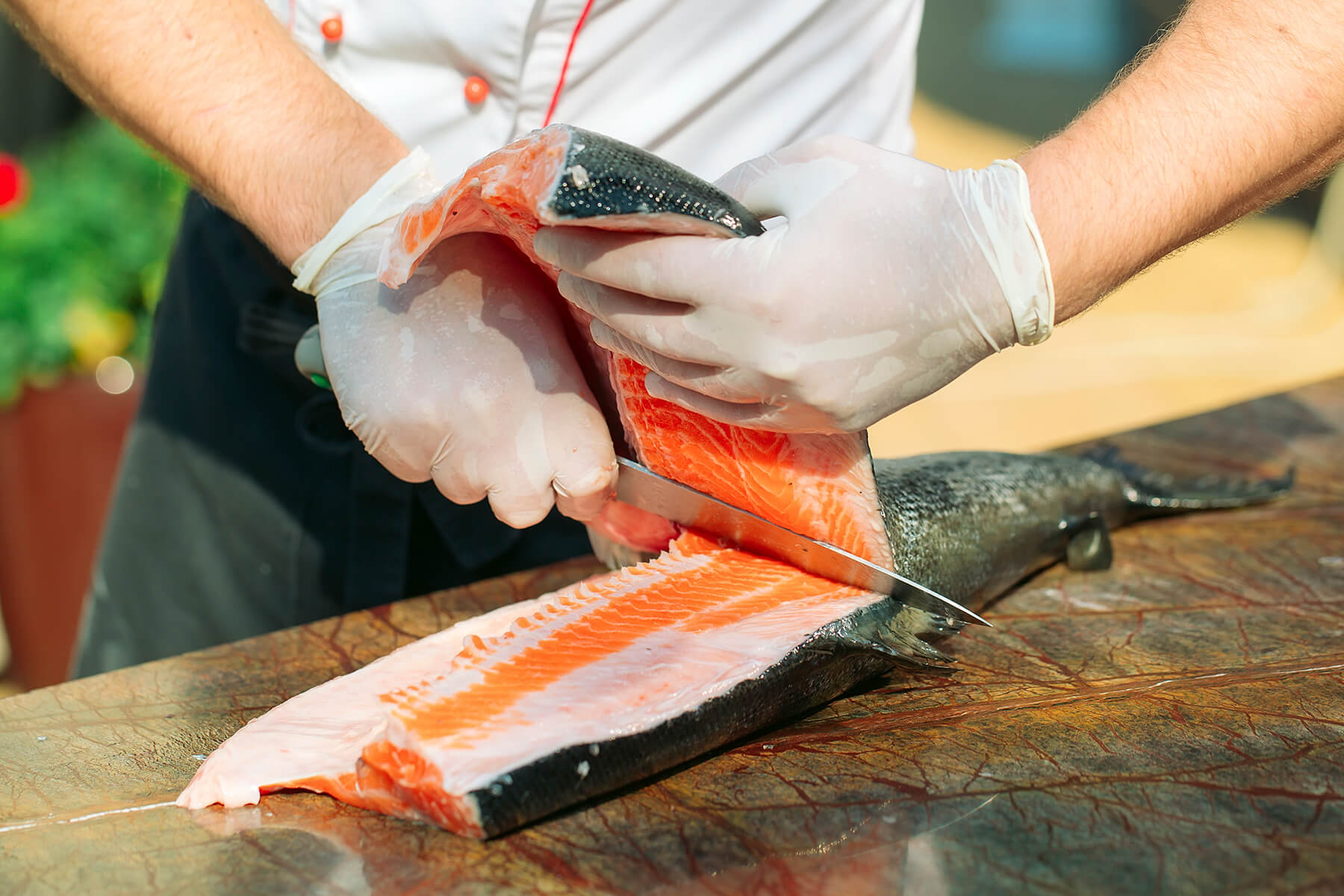 Ein Lachsfilet wird mit einem langen Messer flach am Rückgrat entlang gelöst und mit der zweiten Hand angehoben