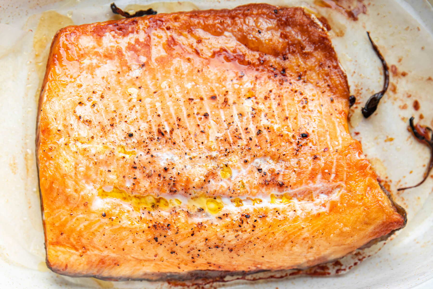 Gebackenes Lachsfilet von oben mit weißen Eiweißflecken entlang der Mittellinie, gelben Fetttröpfchen und grobem Pfeffer