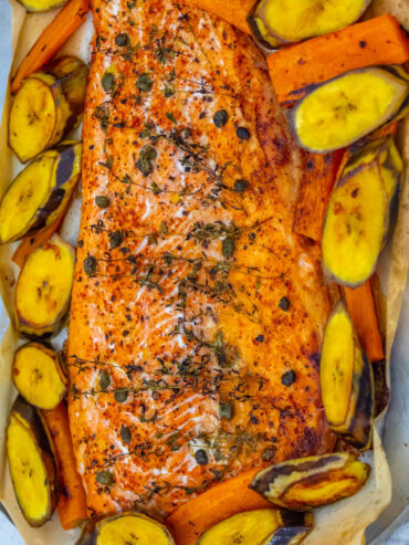 Gebackene Lachsseite mit Thymianzweigen, Kapern und Paprika auf Backpapier, ringsum gebackene Kochbananenscheiben mit Schale und Möhrenstifte
