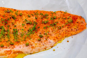 Rohe, mit Paprika und Pfeffer gewürzte Lachsseite mit Thymianzweigen und Kapern auf Backpapier, am Rand Olivenöl