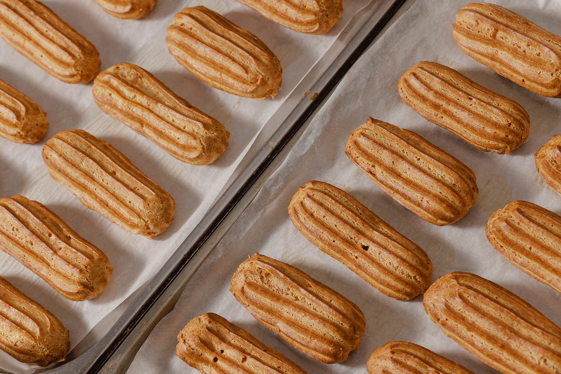 Zwei Bleche mit Backpapier und gleichmäßigen Reihen frisch gebackener Éclairs